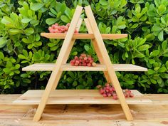 a three tiered wooden shelf with berries on it in front of some green bushes