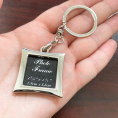 a hand holding a metal frame keychain with a black plaque on it's side