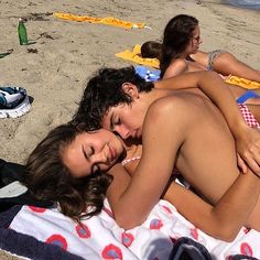 two people are laying on the beach with their arms around each other as they sleep