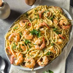 pasta with shrimp and parsley in a white bowl on a gray tablecloth next to silverware