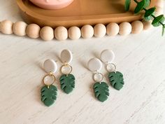 three green and white earrings sitting on top of a wooden table next to a plant