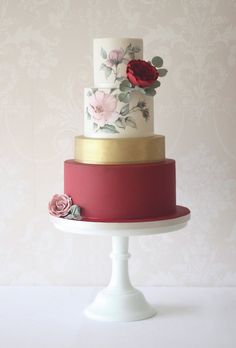 a three tiered cake with red and white frosting on a stand against a wall