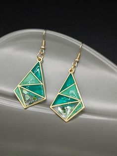 a pair of green and gold earrings sitting on top of a white plate with a black background