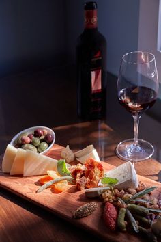 a wooden cutting board topped with different types of cheese and meats next to a glass of wine