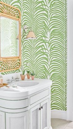 a white sink sitting under a mirror next to a green wallpapered bathroom area