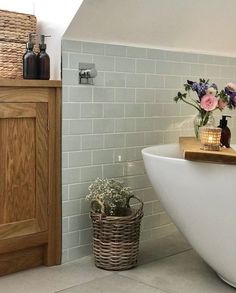 a white bath tub sitting next to a wooden cabinet with flowers in vases on it