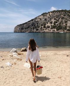 a woman is walking on the beach with a bag in her hand and an island in the background