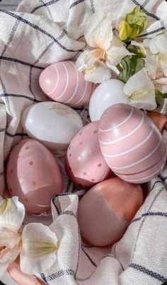 some pink and white easter eggs in a basket with flowers on the table cloth next to them