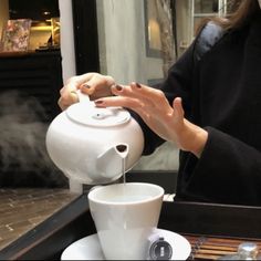 a woman pours coffee into a white teapot with steam coming out of it