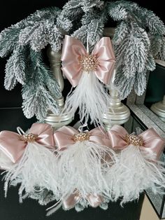 some white feathers and pink bows are sitting on a table next to pine branches with snow