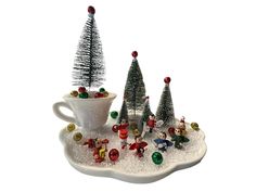 three small christmas trees in a cup and saucer on a platter with candy