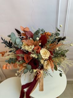 a bouquet of flowers sitting on top of a white table next to a chair with a red ribbon