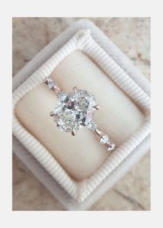 an engagement ring in a white box on a marble counter top, with the center diamond surrounded by smaller diamonds