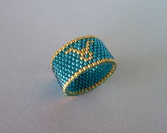 Handmade beaded ring with Zodiac symbol for Taurus. The second sign in my Zodiac beaded ring collection, inspired by my love of astronomy, astrology, mythology and love of bead weaving. Classic style ring design with the Zodiac symbol for Taurus. Symbol and border beads are 24KT gold plate. Center beads are Temple Teal color. Similar to the Aries ring the beads are transparent teal with silver lining. This gives the beads visual depth and reflect the light beautifully. Venus is the ruling planet Beading Rings, Aries Ring, Taurus Symbol, Taurus Zodiac Sign, Seed Bead Projects, Woven Ring, Astrological Signs, Seed Beading, 22 December