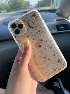 a woman holding up her phone case in the back seat of a car with stars and moon designs on it