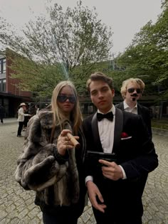 two people dressed in formal wear standing on a cobblestone area with trees and buildings behind them