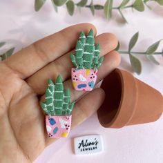 two small pink and green plants are in someone's hand next to a flower pot