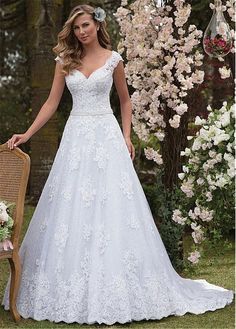 a woman in a wedding dress standing next to a chair with flowers on the back