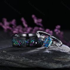 two rings sitting on top of a rock with purple flowers in the background at night