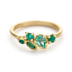 a gold ring with three green stones on the front and two diamonds on the back