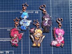 four different anime keychains are on a blue mat with rulers in front of them