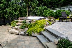 an outdoor hot tub surrounded by stone steps and plants in the back yard with chairs around it