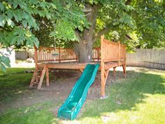 a green slide in the middle of a yard next to a wooden bench and tree