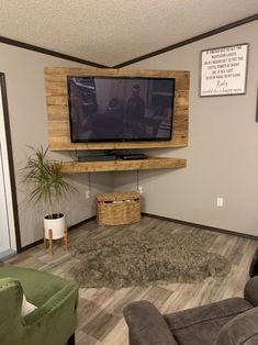 a flat screen tv mounted to the side of a wall in a living room next to two green chairs