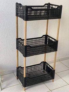 a three tiered shelf with baskets on it in front of a white wall and tiled floor