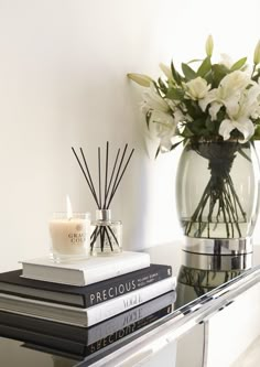 a vase with flowers and candles on top of some books next to a glass table