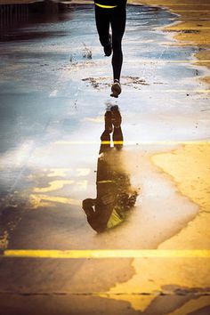 a person is running down the street with their reflection in the wet pavement and buildings behind them