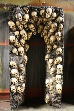 a bunch of skulls that are sitting in front of a door with an arch made out of them