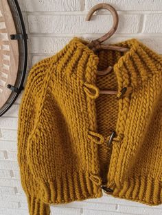 a yellow sweater hanging up against a brick wall next to a wooden rack with hooks