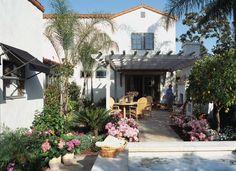 a house with flowers and plants in the front yard, next to an outdoor dining area