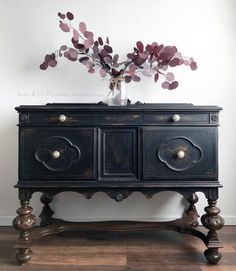 an old black dresser with flowers in it on top of a wooden floor next to a white wall