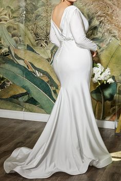 a woman in a white wedding dress standing next to a wall with plants on it