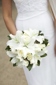 a woman holding a bouquet of white flowers in her hand and wearing a wedding dress