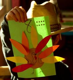 a child holding up a paper turkey cut out to make it look like he is wearing a hat