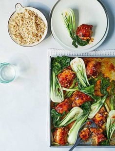 a pan filled with meat and vegetables on top of a table next to bowls of rice