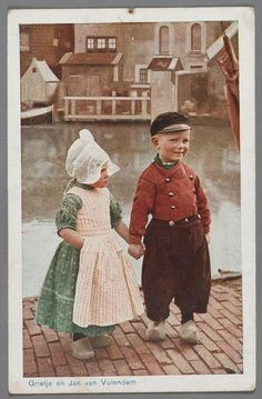 two children are holding hands on a brick walkway near water and houses in the background