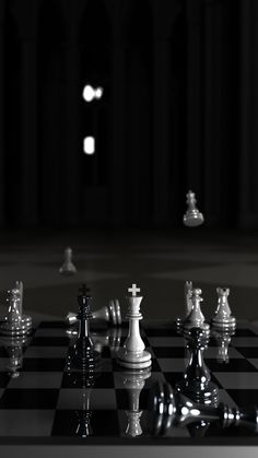 a black and white photo of chess pieces on a checkerboard floor with lights in the background