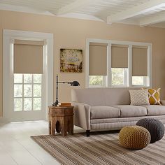 a living room filled with furniture and windows covered in roman shades on top of them