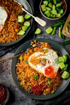 two plates filled with rice and vegetables on top of a gray tablecloth next to silver spoons