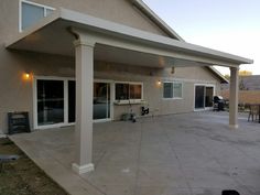 an outdoor patio with white pillars and lights on the ceiling, next to a house