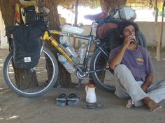 a man sitting on the ground next to a bike and drinking from a water bottle