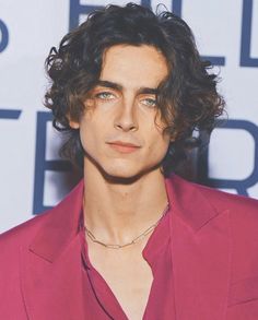 a man with curly hair wearing a pink suit