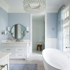 a white bath tub sitting next to a bathroom sink under a large round light fixture