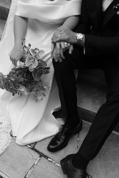 a bride and groom sitting on the steps holding each other's hands with flowers in their lap