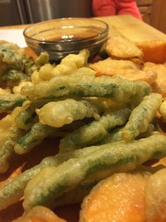 green beans and other food items on a wooden table next to a bowl of dipping sauce