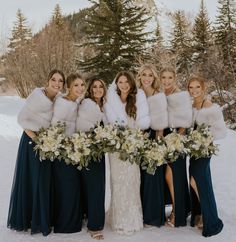 a group of women standing next to each other in front of snow covered trees with fur stoles